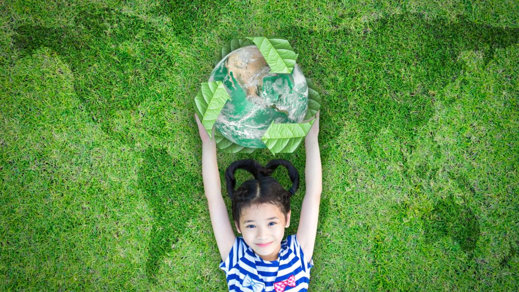 Menina deitada na relva a segurar um símbolo ecológico