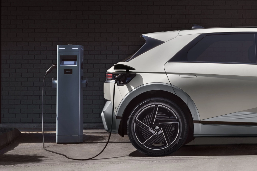 Carro elétrico Hyundai branco ligado a posto de carregamento junto à parede escura.